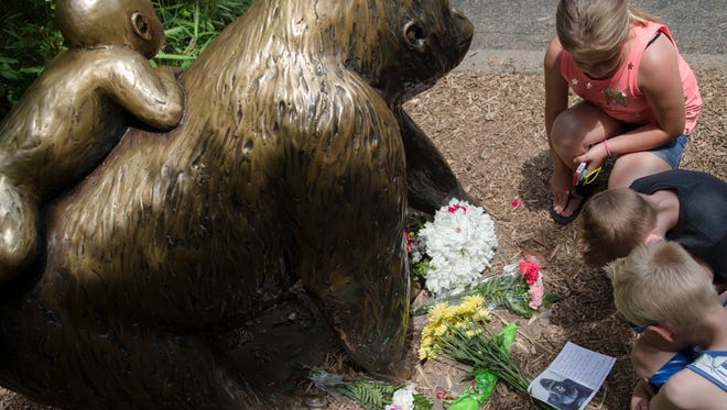 Children pause at the feet of a gorilla statue where flowers and a sympathy card have been placed, outside the Gorilla World exhibit at the Cincinnati Zoo & Botanical Garden, Sunday, May 29, 2016, in Cincinnati. On Saturday, a special zoo response team shot and killed Harambe, a 17-year-old gorilla, that grabbed and dragged a 4-year-old boy who fell into the gorilla exhibit moat. Authorities said the boy is expected to recover. He was taken to Cincinnati Children's Hospital Medical Center.