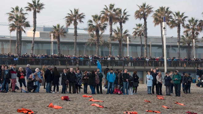 People stand past life jackets spread on the beach during a demonstration to demand to welcome refugees in Barcelona on Feb. 18, 2017.
