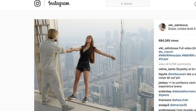 A video taken of the incident shows Viki Odintcova, 23, lean off the ledge of a skyscraper as a male assistant holds her hand, and later dangling off of the 1,004-foot-high Cayan Tower.
