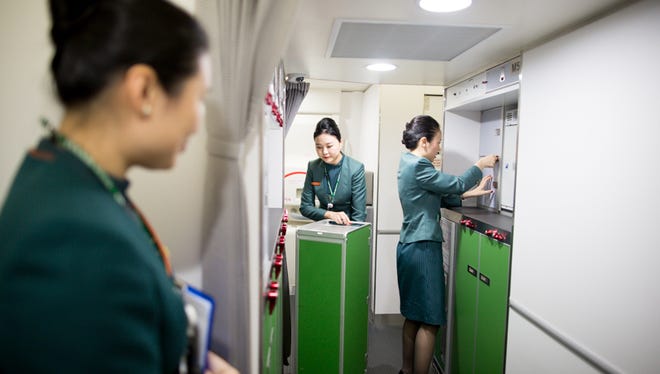 An instructor keeps a watchful eye over a pair of flight attendant trainees, who are practicing pre-arrival cabin and galley prep.