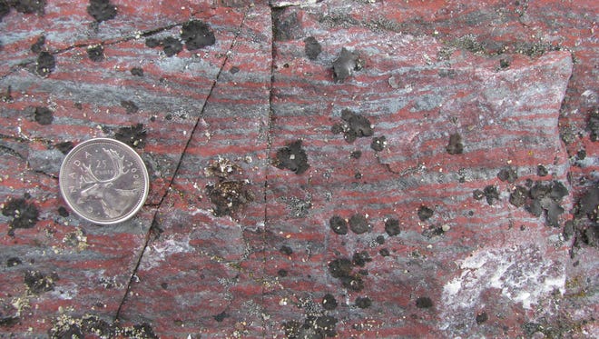 Jasper banded iron formation from the Nuvvuagittuq Supracrustal Belt in Quebec, Canada, with grey magnetite layers and red haematite-rich silica layer, both being iron- oxide minerals. Black spots are lichens.